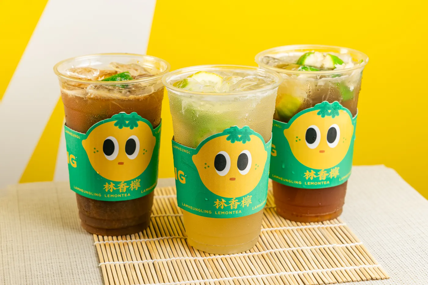 Three Lam Heung Ling lemon teas in green mascot sleeves on a bamboo mat